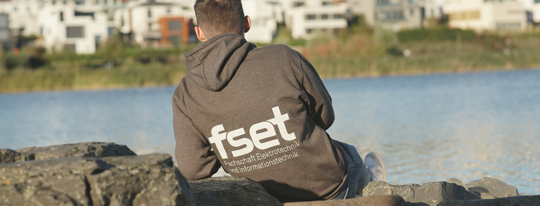 FSR-Mitglied von hinten am Ufer sitzend, Pullover ist hinten mit Logo bedruckt